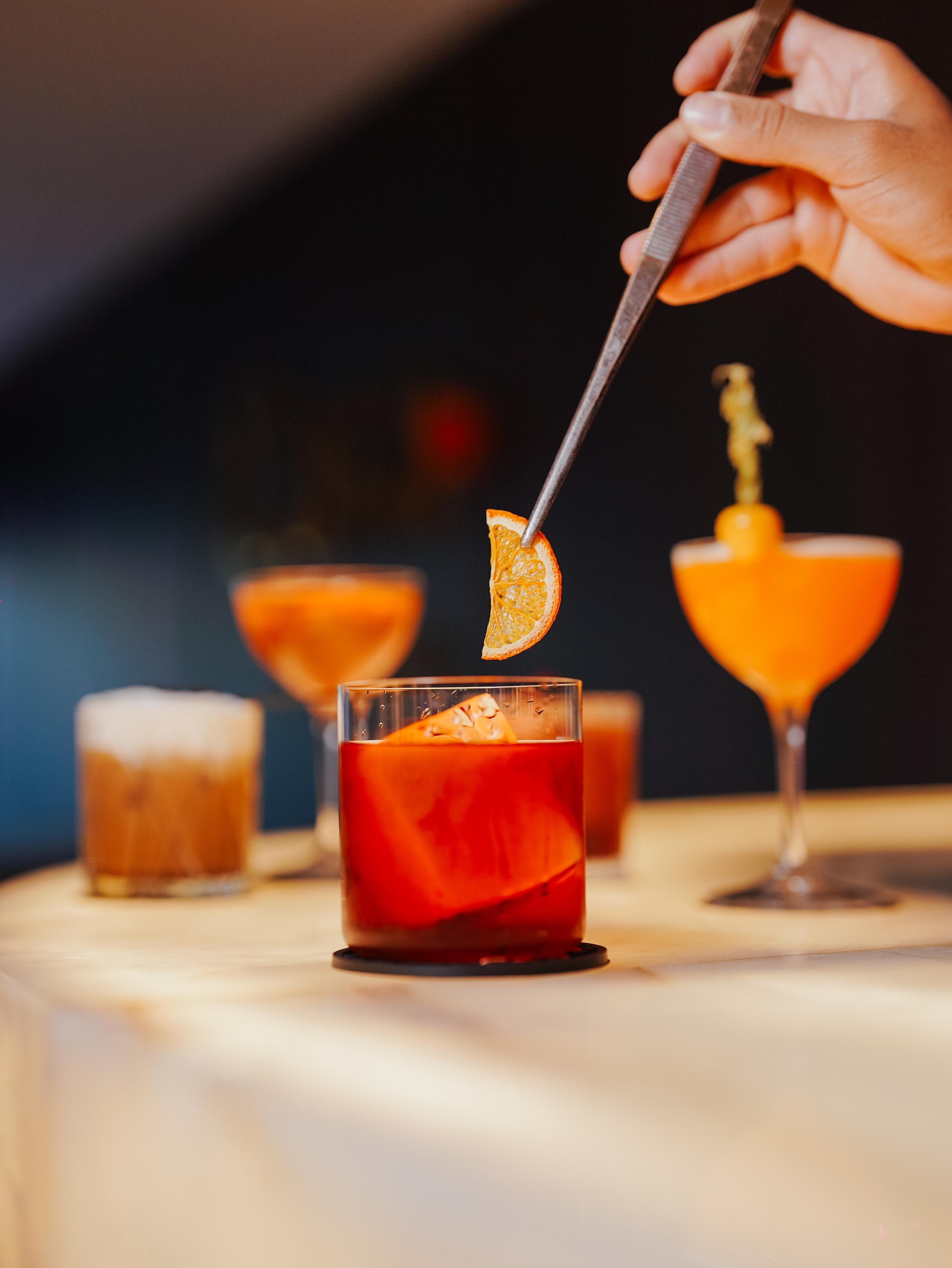 Bartender da Casa Pro Coquetéis finalizando um coquetel autoral com uma rodela de laranja desidratada